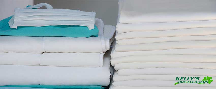 KDC Stack of folded white linens and green surgery clothes