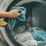 A person putting a blue cloth in the washing machine. | KDC